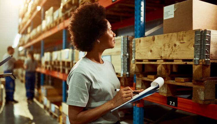 Trabalhador afro americano escrevendo lista de inventário enquanto verifica o estoque na sala de armazenamento